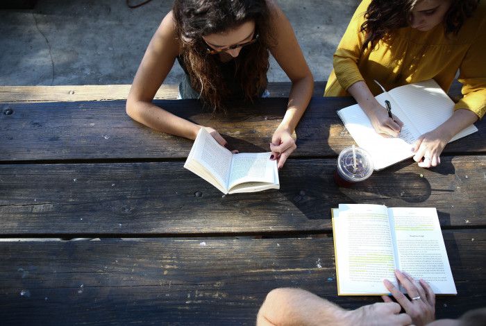 3 friends sitting outside reading and writing together