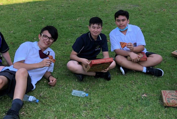 5 teenage boys sat on the grass eating pizza
