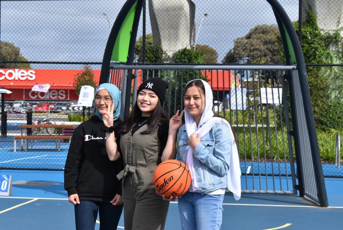 three girls on a basketball court posing while one is holding a basketball