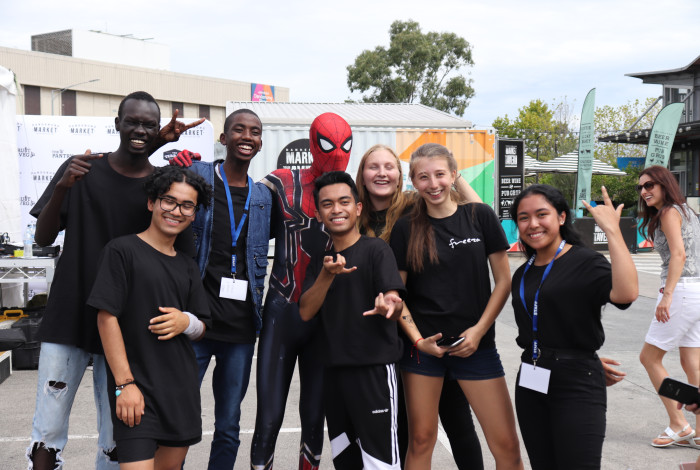 Seven young people posing for a group photo with a spiderman character