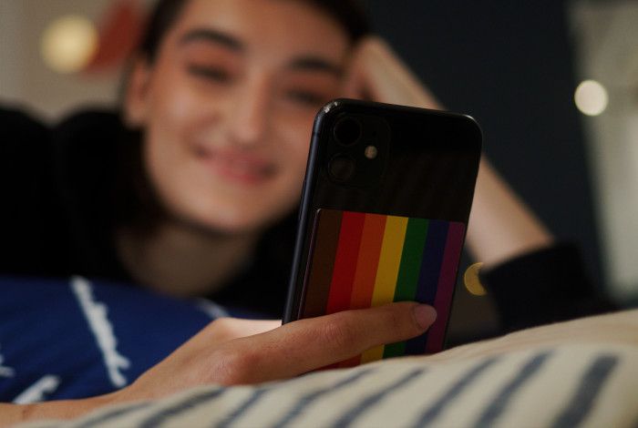 Young person lying on bed on the phone which has a rainbow flag sticker