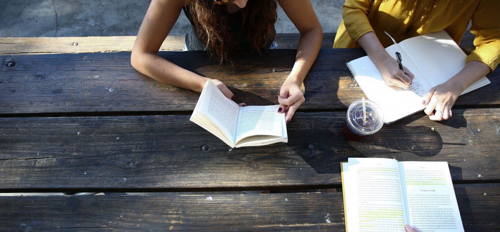 3 friends sitting outside reading and writing together
