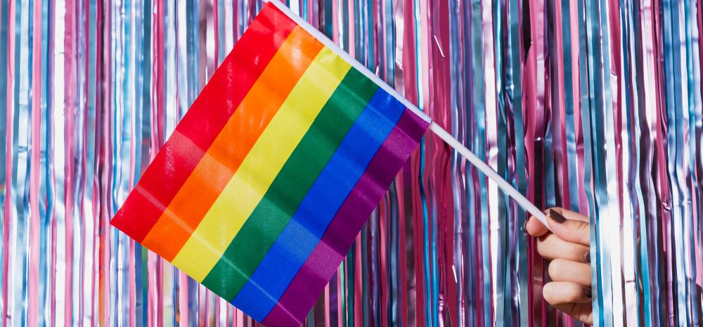 pride flag hold by a hand showing from glittery background