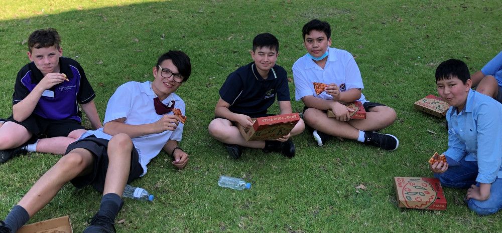 5 teenage boys sat on the grass eating pizza