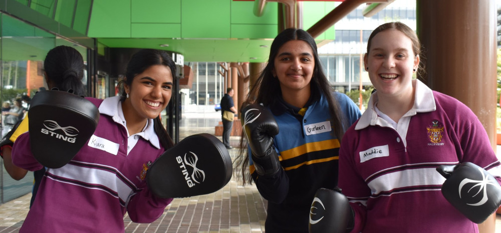 Three young people posing for a photo with boxing gloves and boxing pads on their hands.