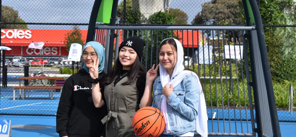 three girls on a basketball court posing while one is holding a basketball